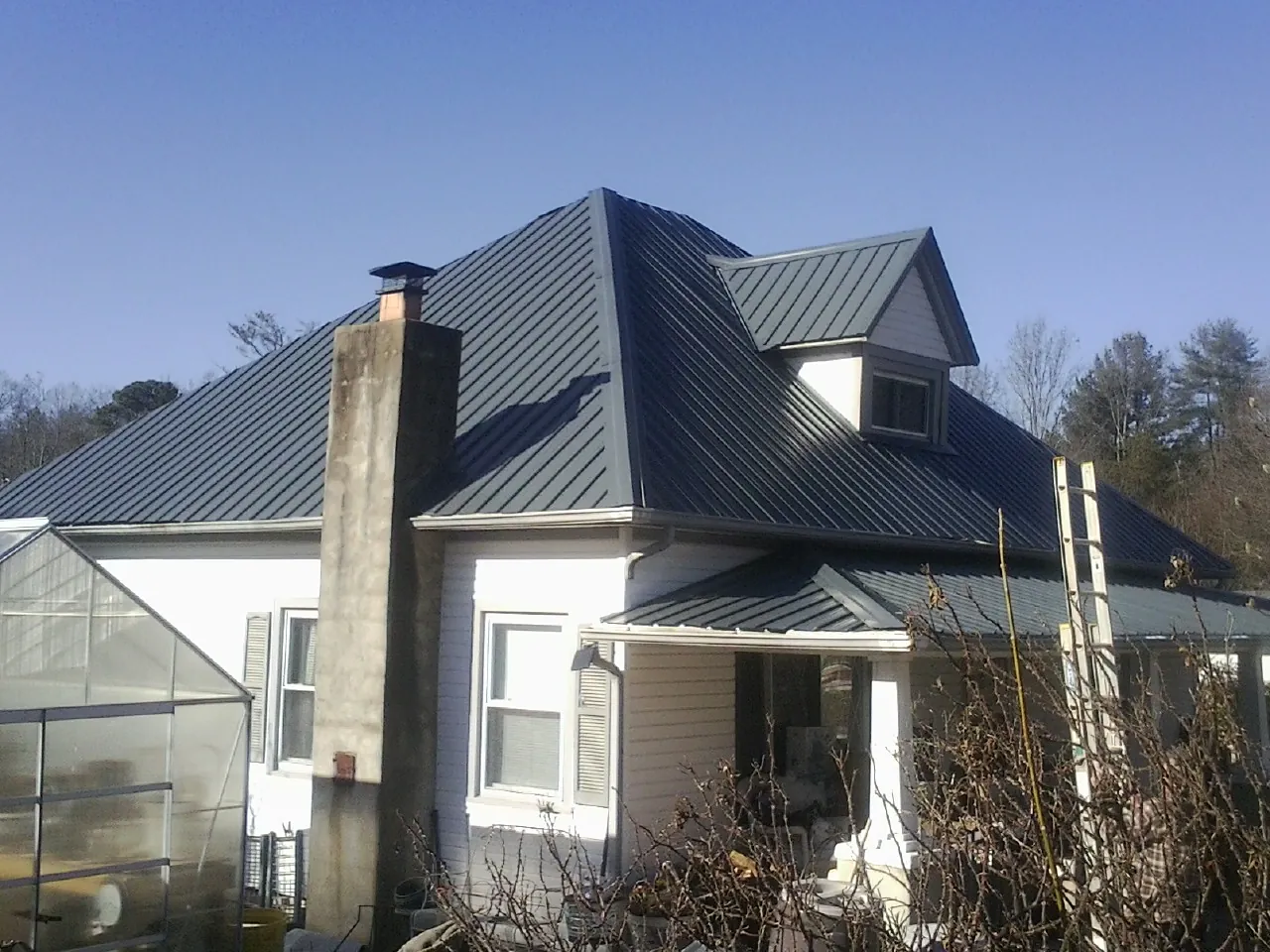Dark blue standing seam metal roof on a white farmhouse with dormer — Slate & Tile Roof Repair by Roofing Brothers in Carrollton