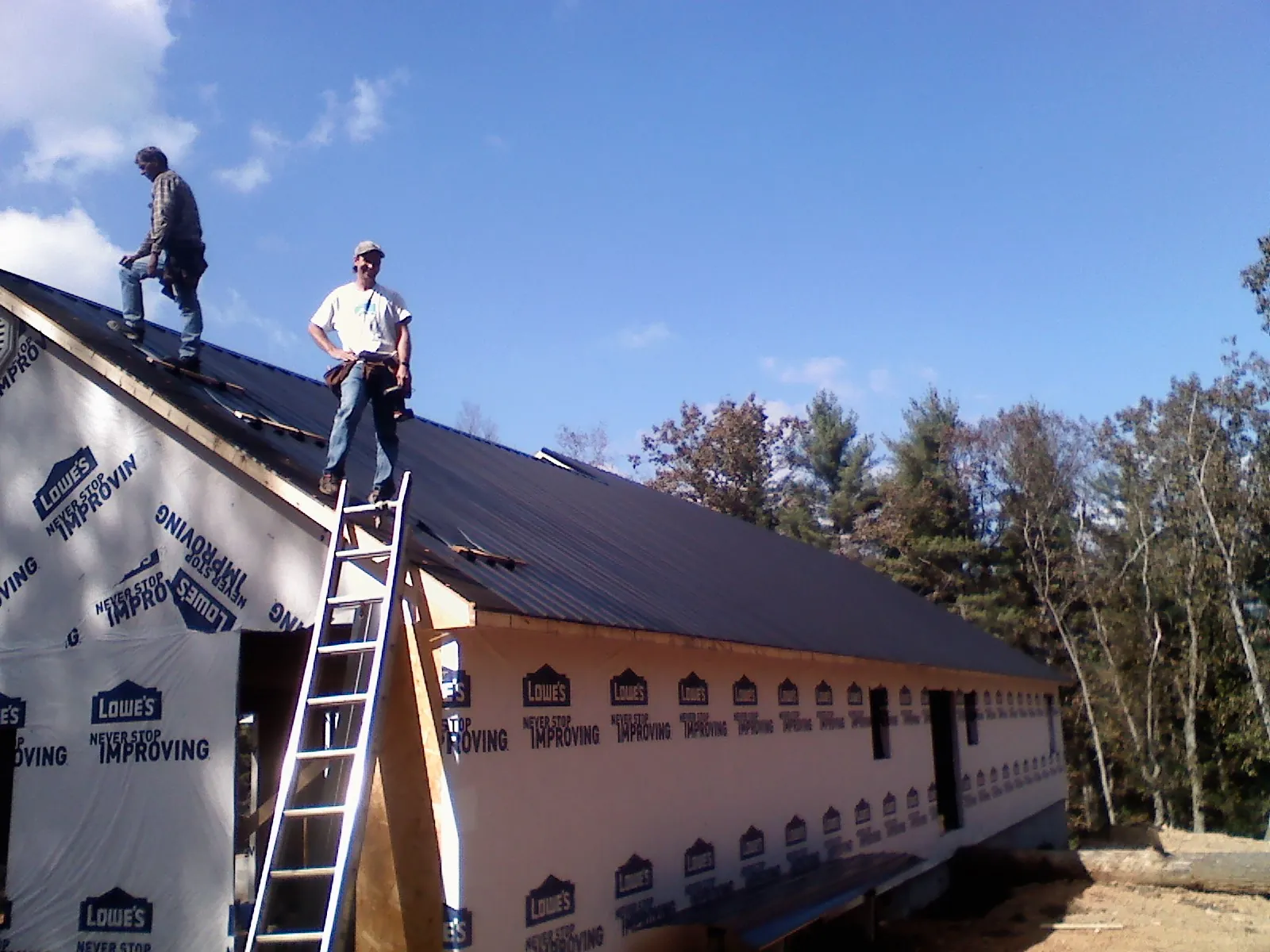 Two roofers standing on a long dark metal roof over a wrapped building in Carrollton